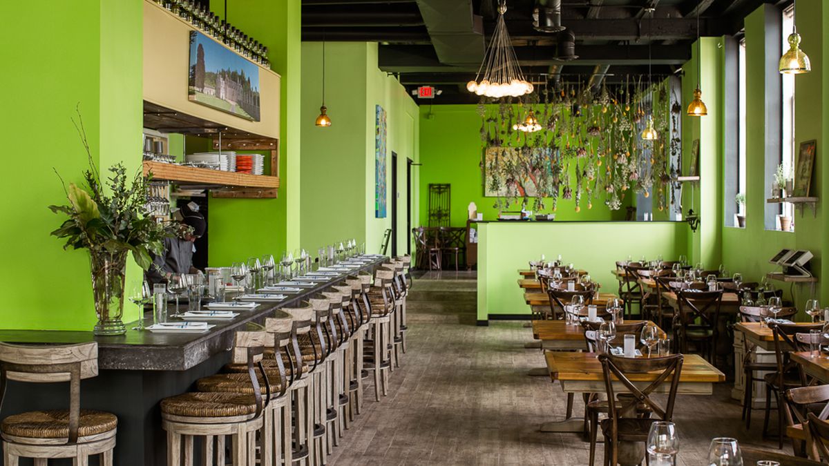 The interior of Chartreuse Kitchen &amp; Cocktails with green walls, tables, chairs, a bar, and barstools.
