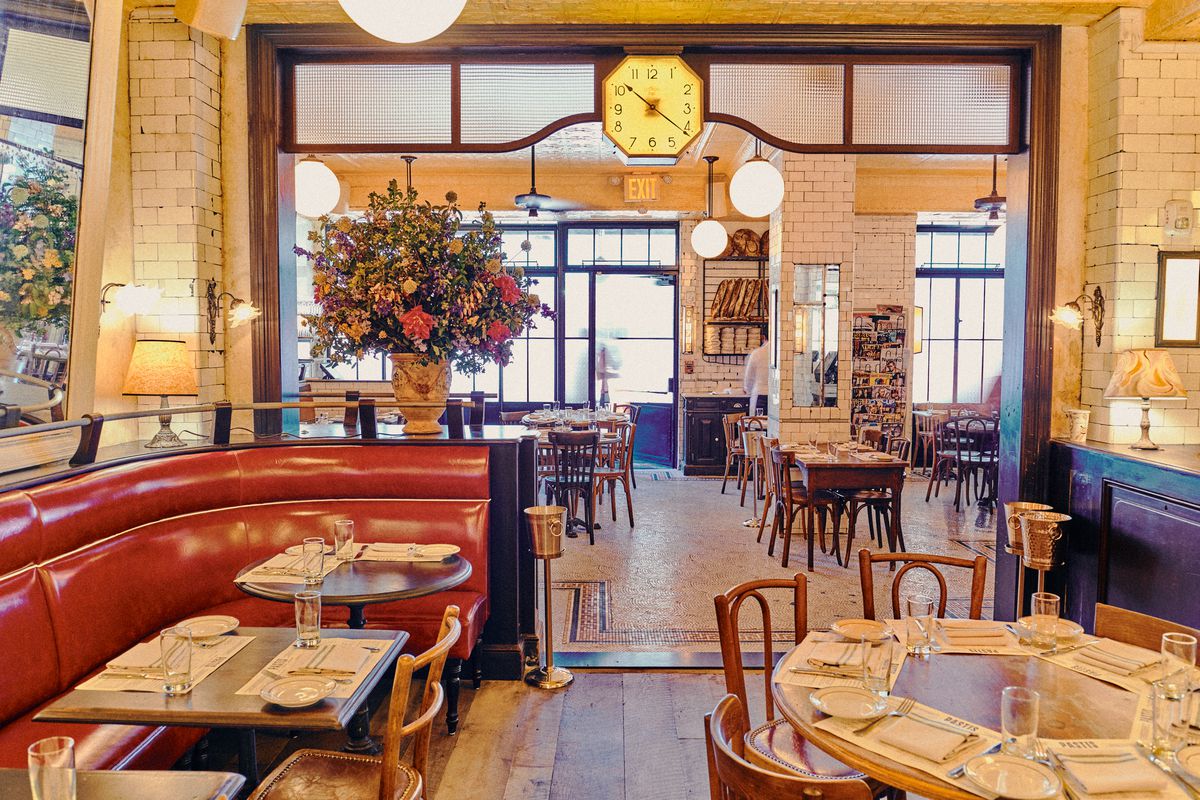Pastis’s dining room has a clock in the middle, brown-red banquettes to the left, and a large vase of flowers.
