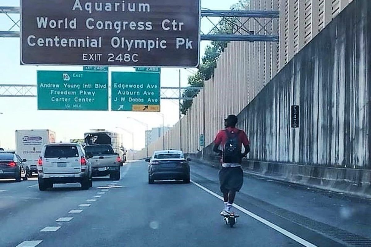 A photo of a man riding a Bird scooter on the highway