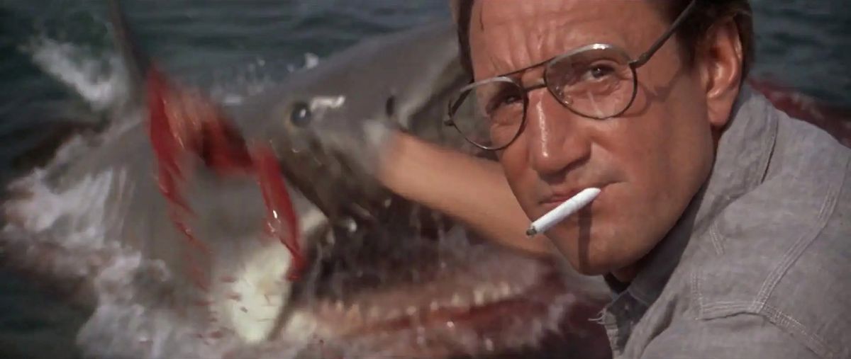 Roy Scheider as Martin Brody scooping chum into the ocean, unaware of the great white shark surfacing in the water in Jaws.