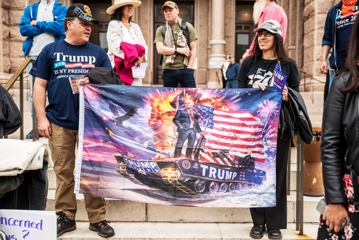 Protesters wearing Trump t-shirts hold a flag bearing an image of President Donald Trump on a tank in front of an American flag. They’re standing on the steps of the Texas State Capitol building on April 18, 2020 in Austin, Texas, where protesters have gathered to call for the country to be opened up despite the risk of COVID-19.