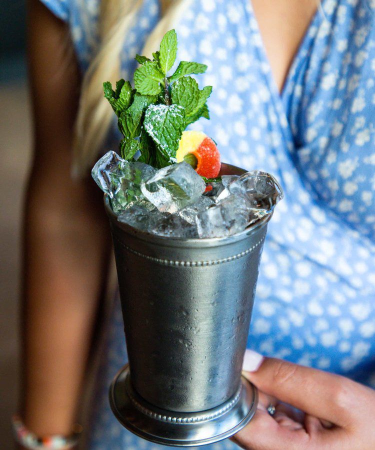 A cocktail with ice and mint greens in a silver metal cup.