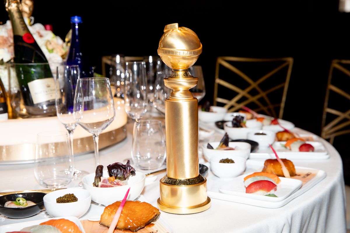 A Golden Globe statue standing on a dining table with a white tablecloth, dishes of food, and a bottle of champagne.
