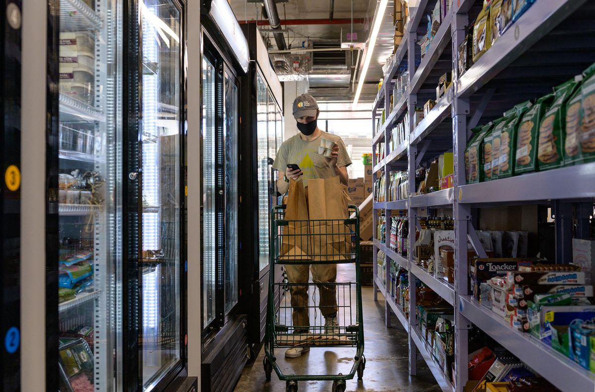 An employee walks down an aisle of a Fridge No More warehouse, gathering grocery items for delivery.