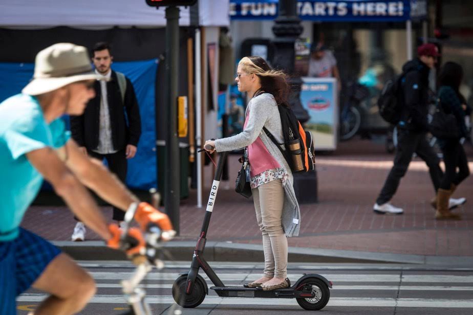 Woman riding shareable scooter down street.