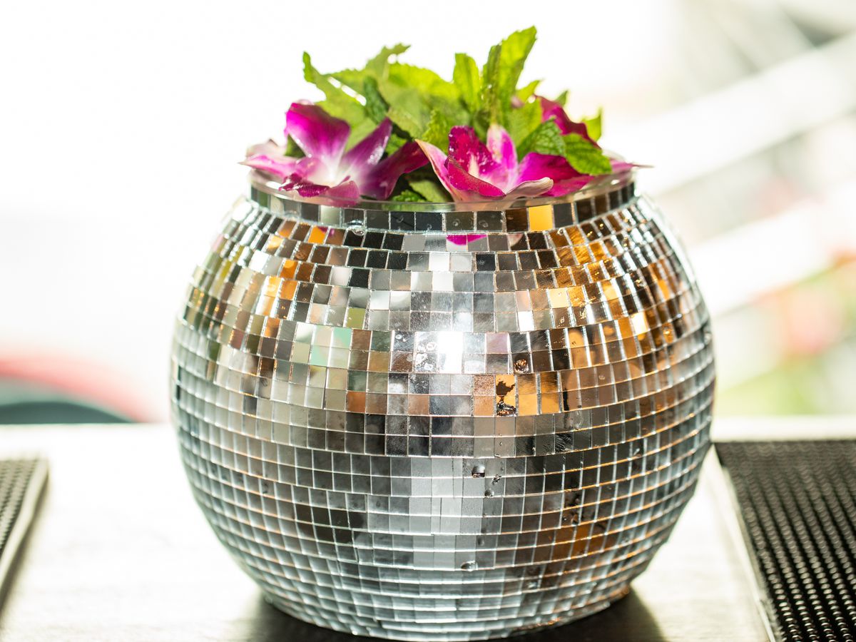 A cocktail served in a glimmering disco-style cup, topped with hibiscus and mint.