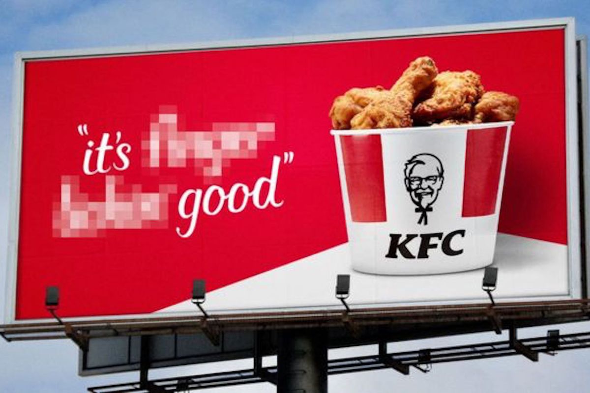 A red and white billboard for KFC fried chicken on a blue sky background, featuring its Colonel brand character and a bucket of chicken, with the “it’s fingerlickin’ good” slogan blurred out to read “it’s good”