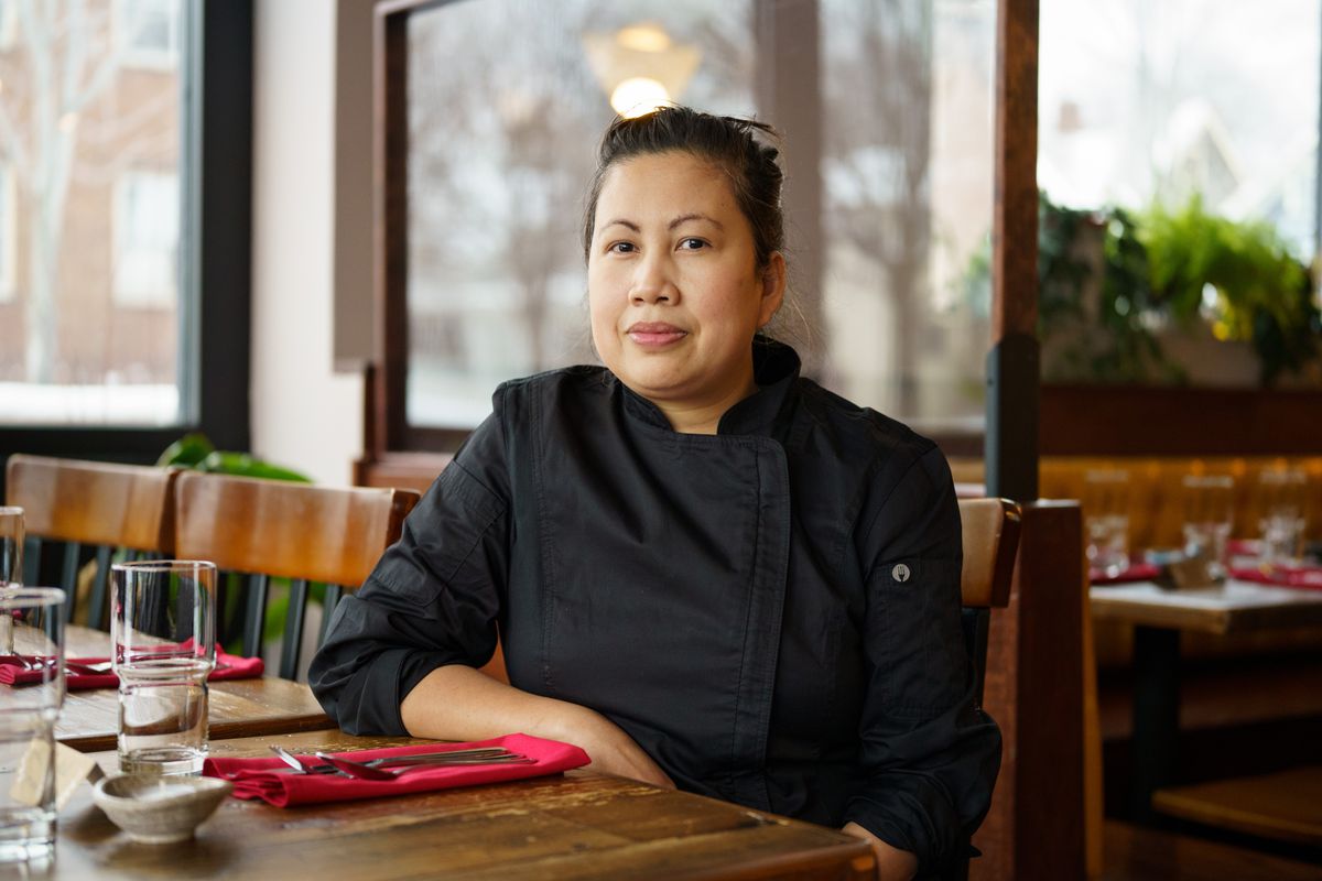 Leah Raymundo, dressed in a black chef coat, sits at a table in her restaurant, Kalsada. 