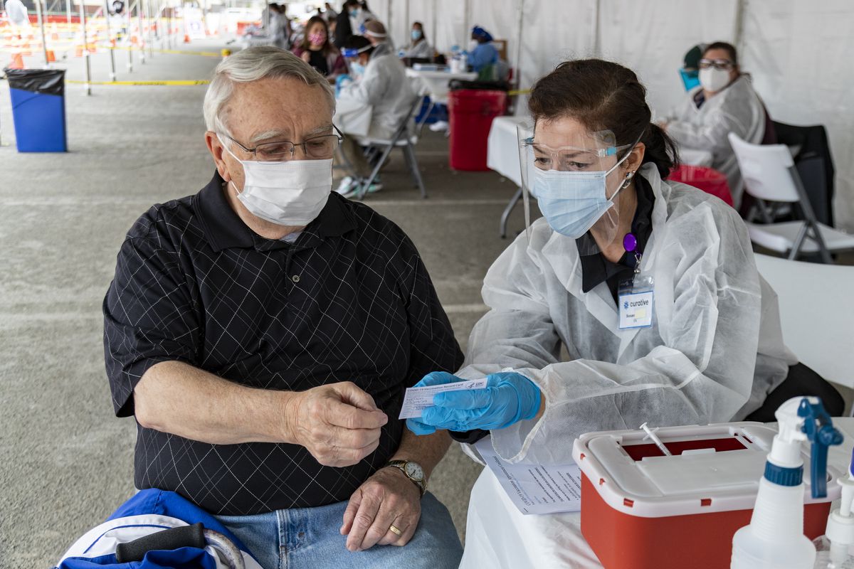 A health care worker in protective gear hands a card to a patient at an outdoor vaccination site in Riverside, California.
