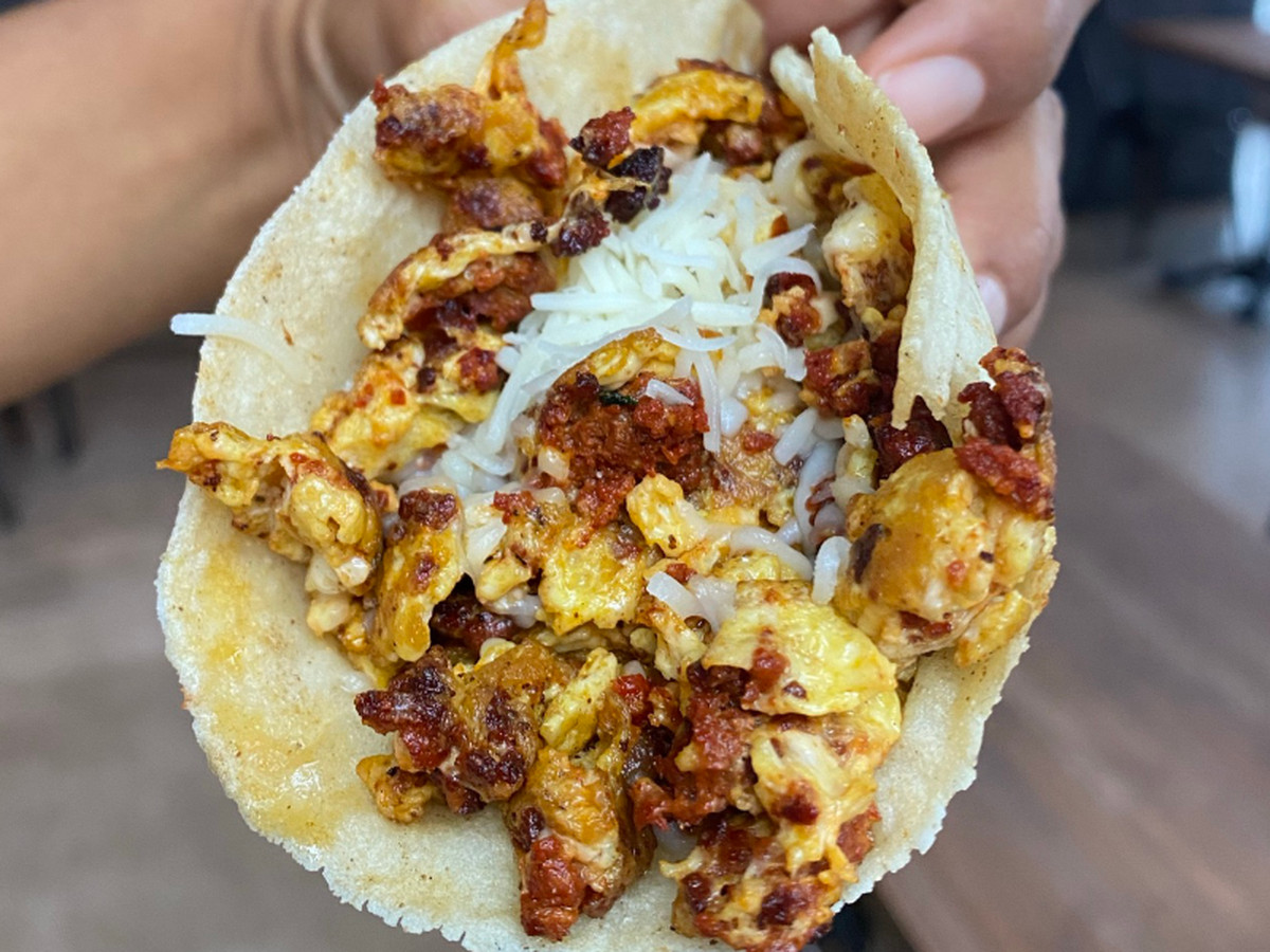 A taco with eggs, meats, and shredded white cheese.