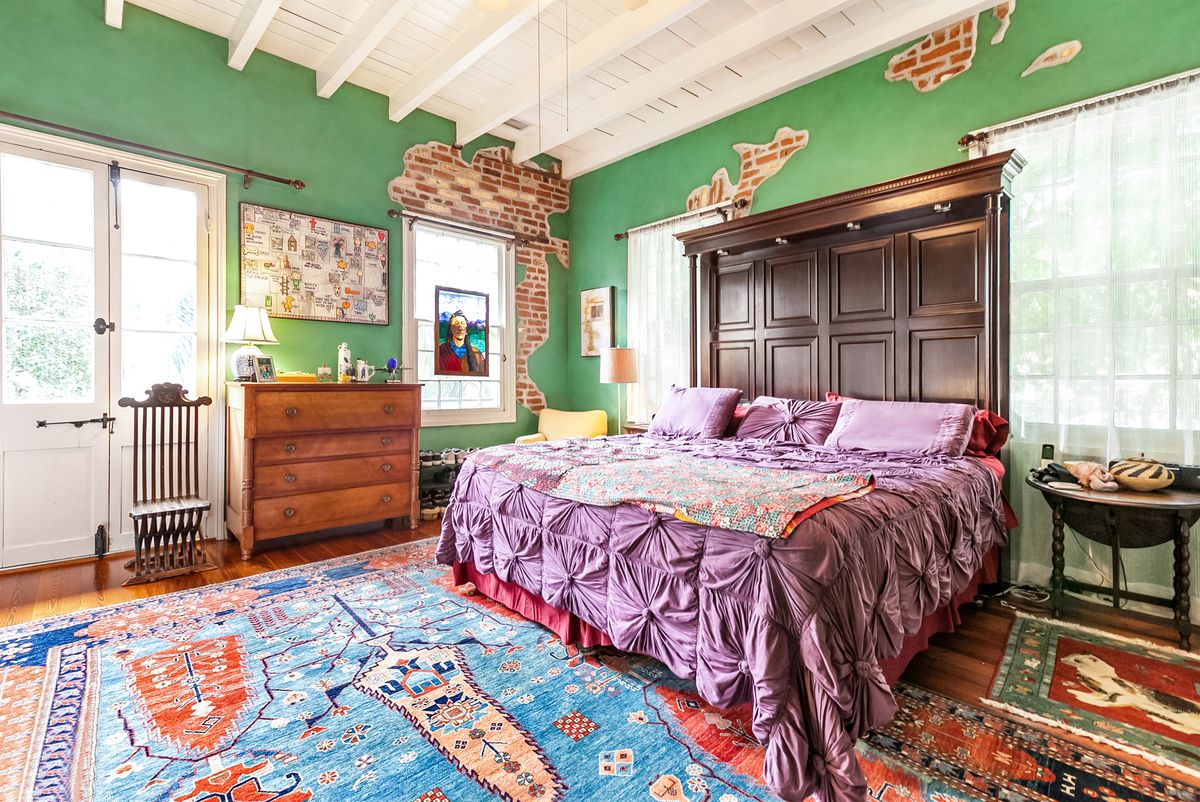 Colorful bedroom with green walls peeling to exposed brick, ceiling beams and a massive bed with wooden headboard