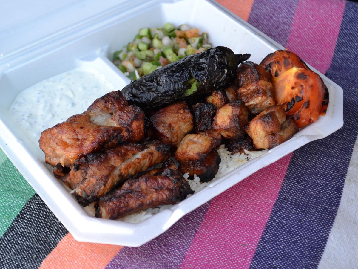 Armenian lunch truck pork ribs and pork belly kebabs in a tray with yogurt sauce and cucumber salad.