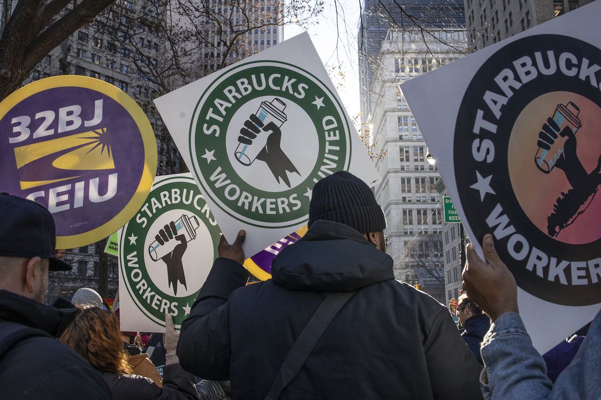 People in winter wear stand outside holding signs reading “Starbucks Workers United.”