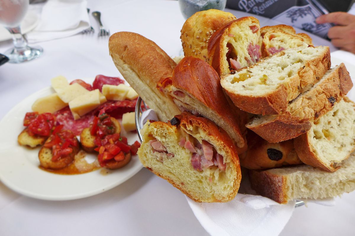 A basket bulging with bread and a smaller plate with sliced salami, cubed cheese, and red pepper topped toasts.