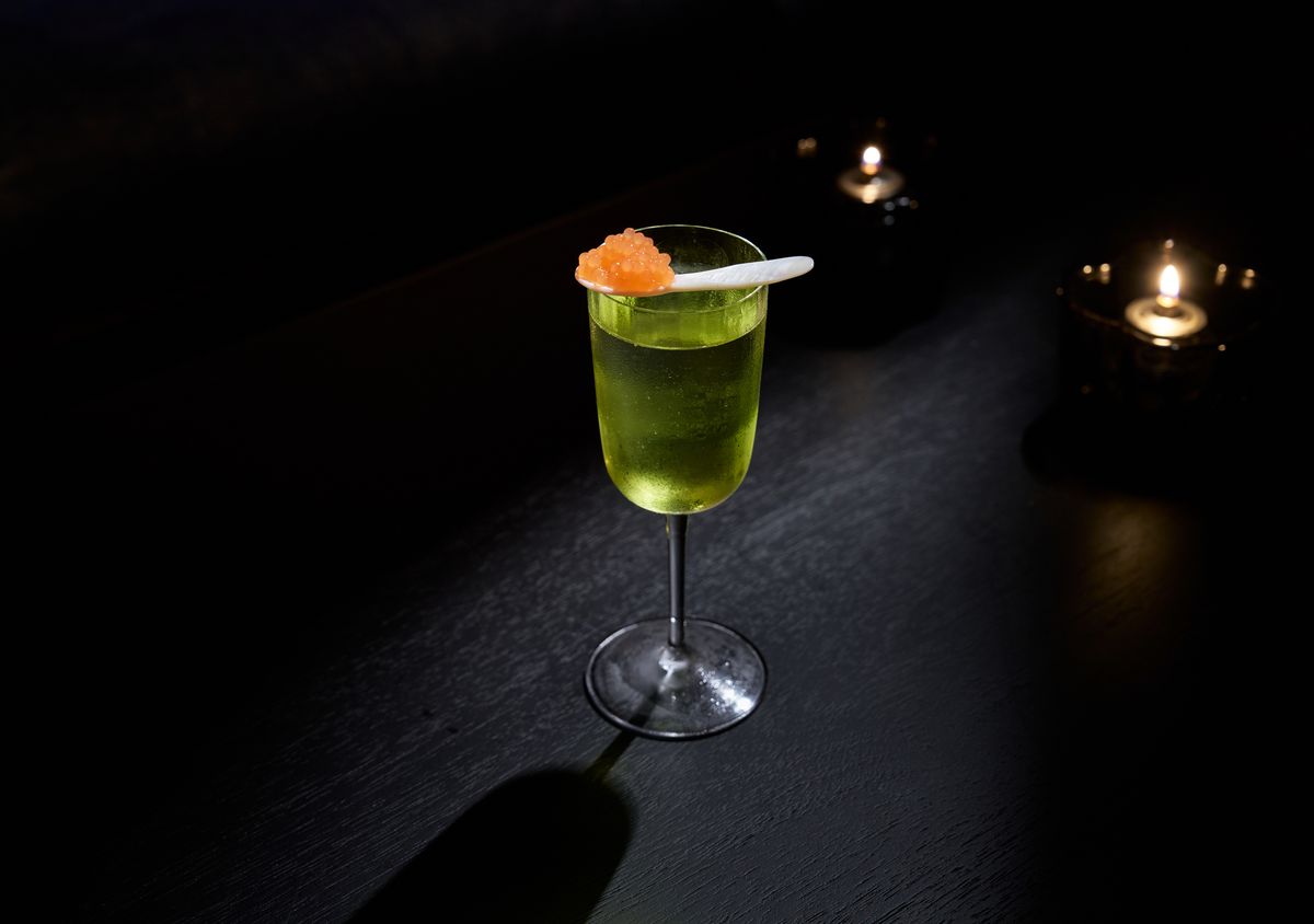 A cocktail with green liquid and a spoon of orange dots.