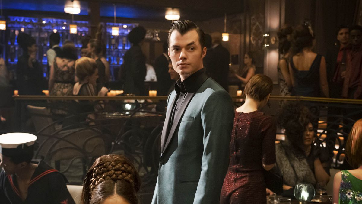 Pennyworth in a nice suit looks around a bar