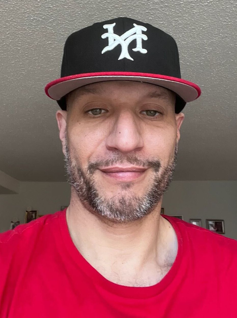 Ariel Beltran, a man with medium-toned skin, a black baseball cap, and a red shirt.
