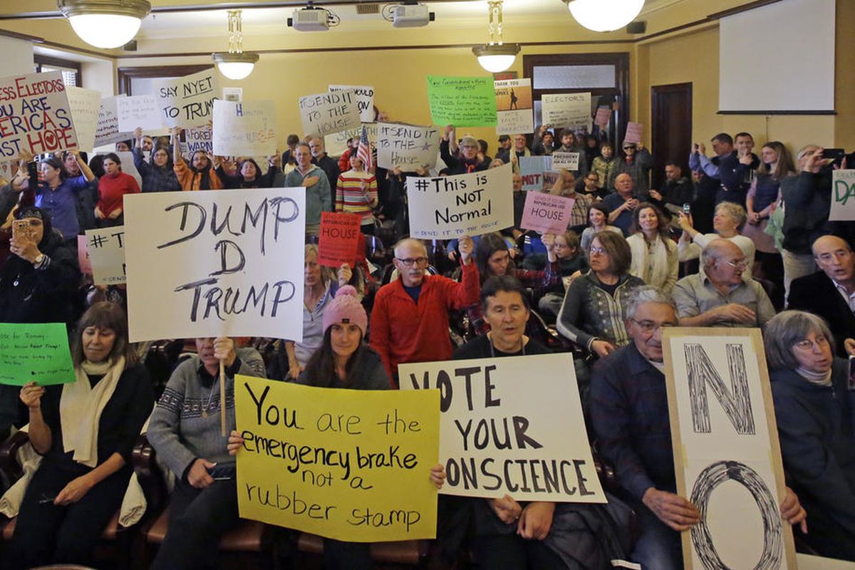 Protesters holds signs as Utah's six presidential electors prepare to cast their votes for President-elect Donald Trump, Monday, Dec. 19, 2016, in Salt Lake City. The six electors, who were chosen by Utah GOP delegates earlier in the year, cast their vote