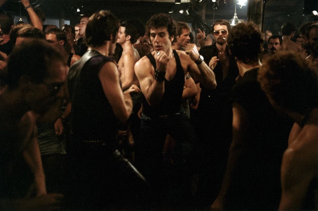 Al Pacino, in jeans and a black sleeveless T-shirt, dances in a crowd of men at a gay bar in Cruising.