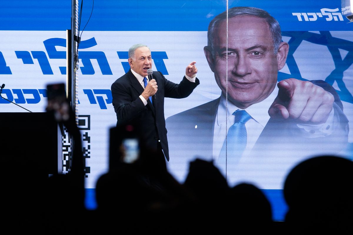 Benjamin Netanyahu speaking from a stage behind which is a large picture of his face and pointing finger.