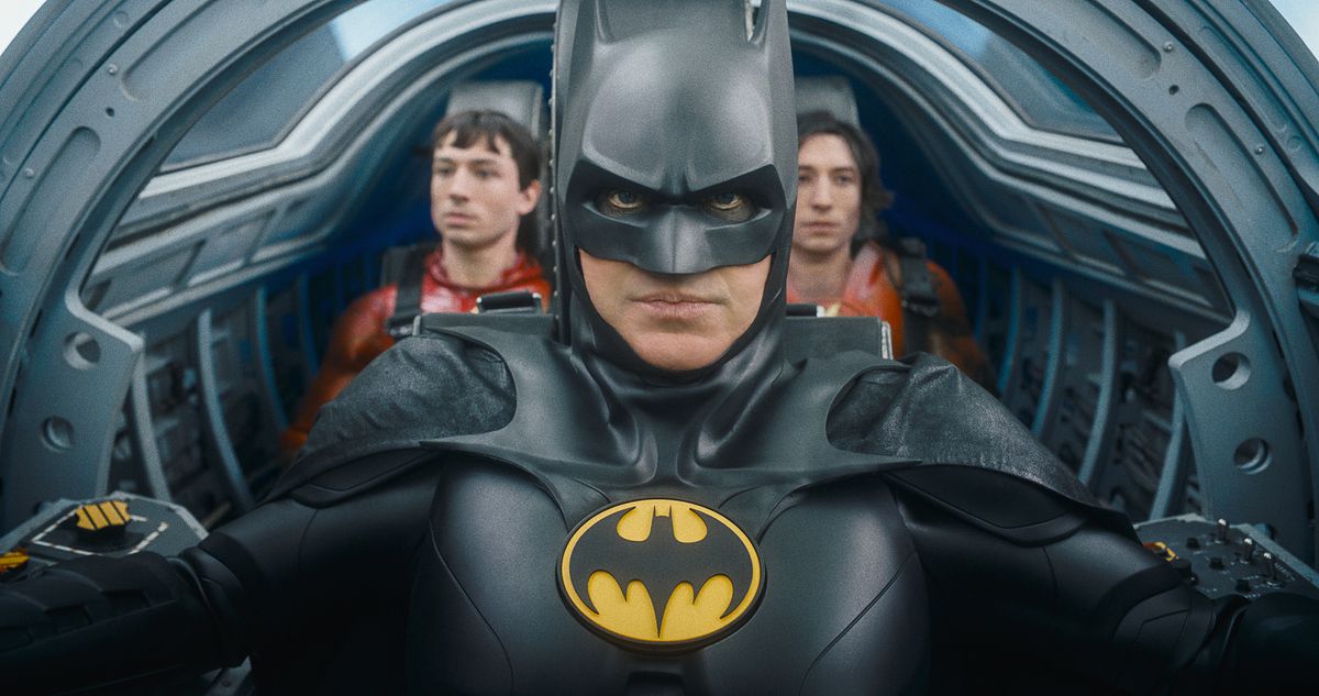 (L-R) Ezra Miller as The Flash, Michael Keaton as Batman and Ezra Miller as The Flash in The Flash. They’re in the cramped cockpit of the Batwing, with Batman in the pilot’s seat and the two Flashes sitting next to each other behind him.