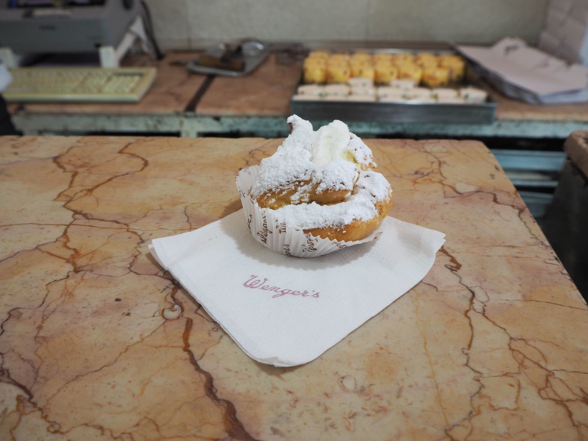 A sugar-dusted pastry sits on a napkin on a marble counter