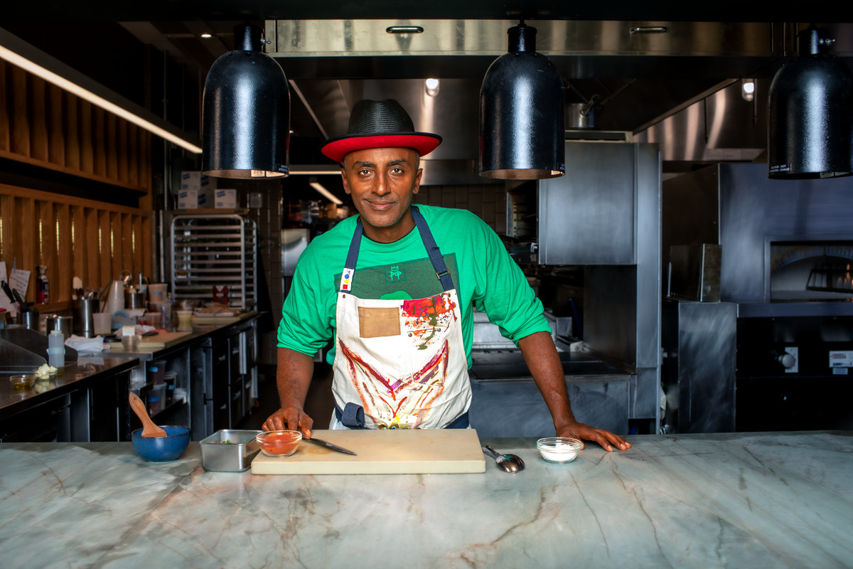Marcus Samuelsson leans over a cutting board on a counter.