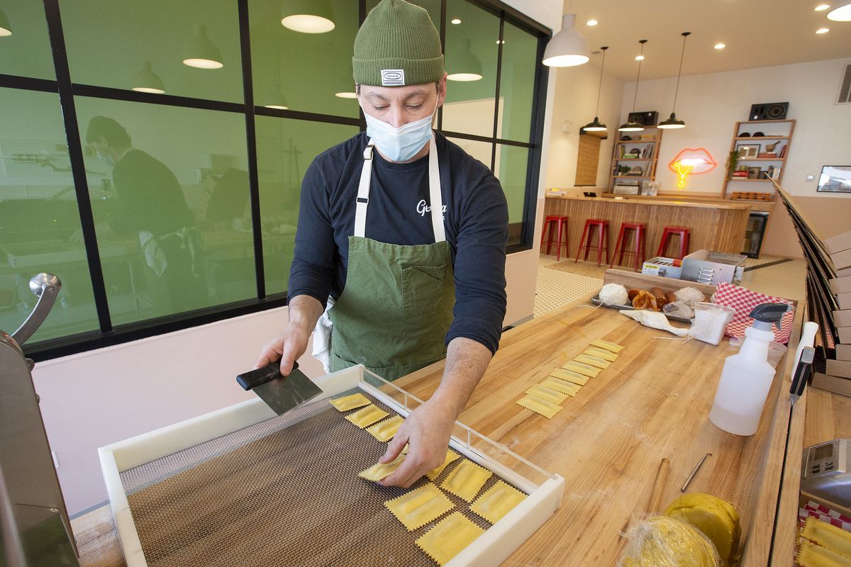 A man in a facemask and a beanie lays individual ravioli on a tray.