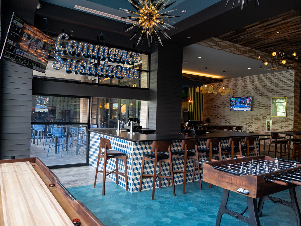 Interior look of a sports bar with ample bar seating, light-up signs, a chandelier, and foosball tables.