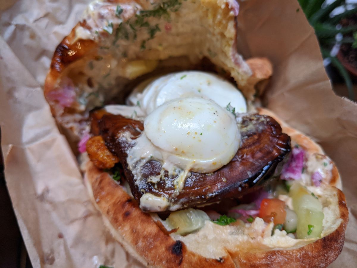A soggy pita split open with sliced eggplant and sliced egg on top of it.