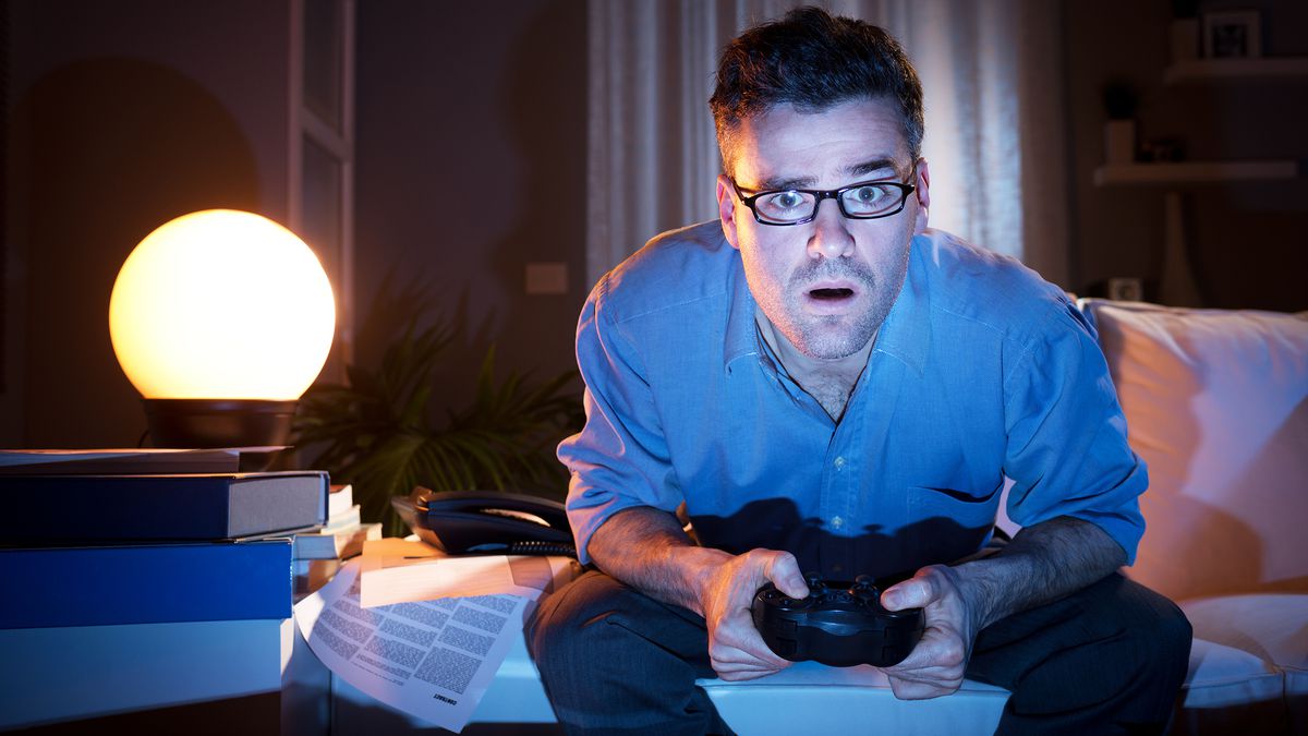 man playing video games at night on messy sofa