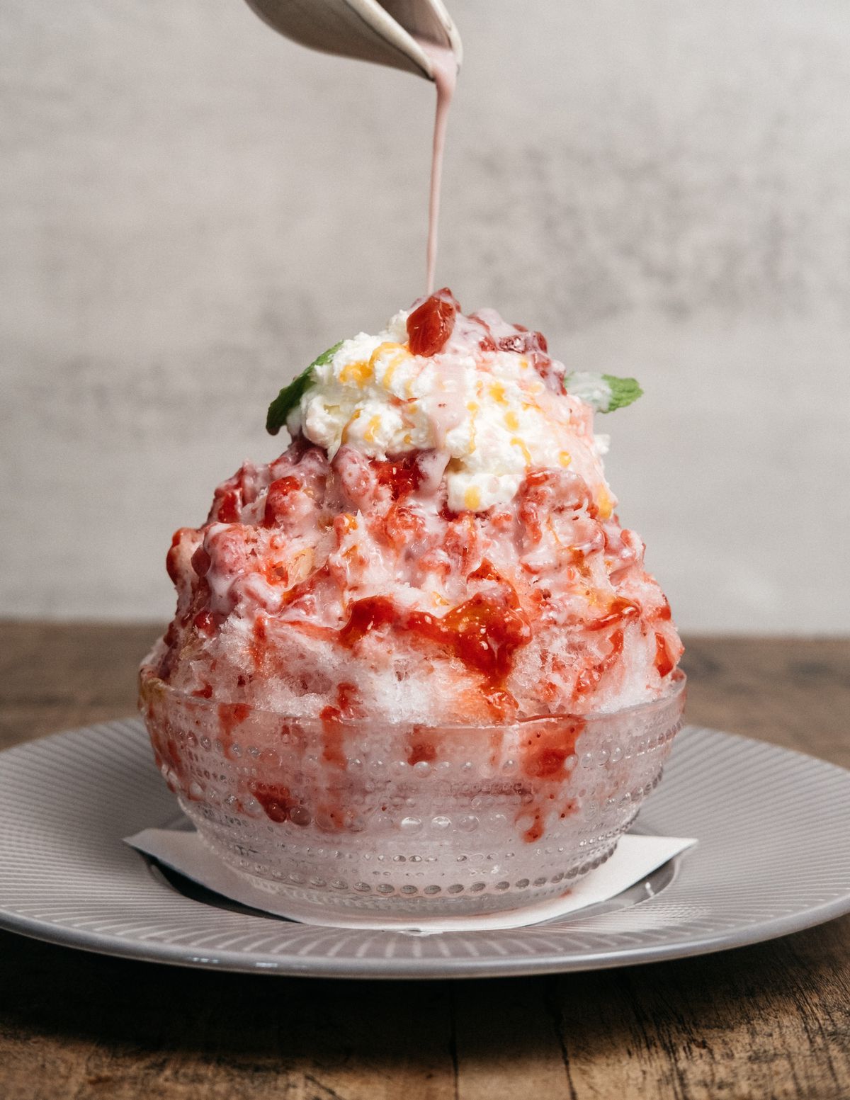 A bowl of katami strawberry kakigori topped with whipped cream, strawberry mint sauce and a drizzle of creamy pink sauce.