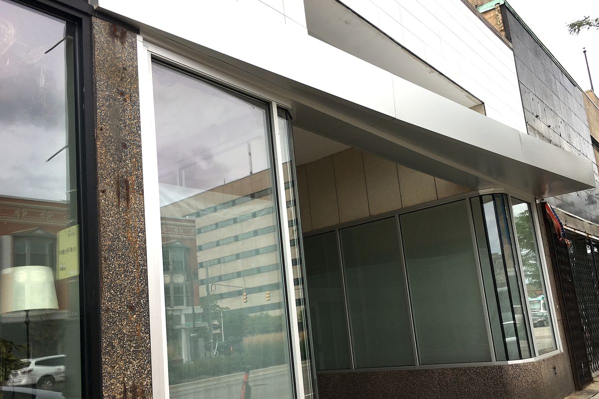 Large windows and a metallic angled panel hanging over the sidewalk on Woodward on a cloudy day.