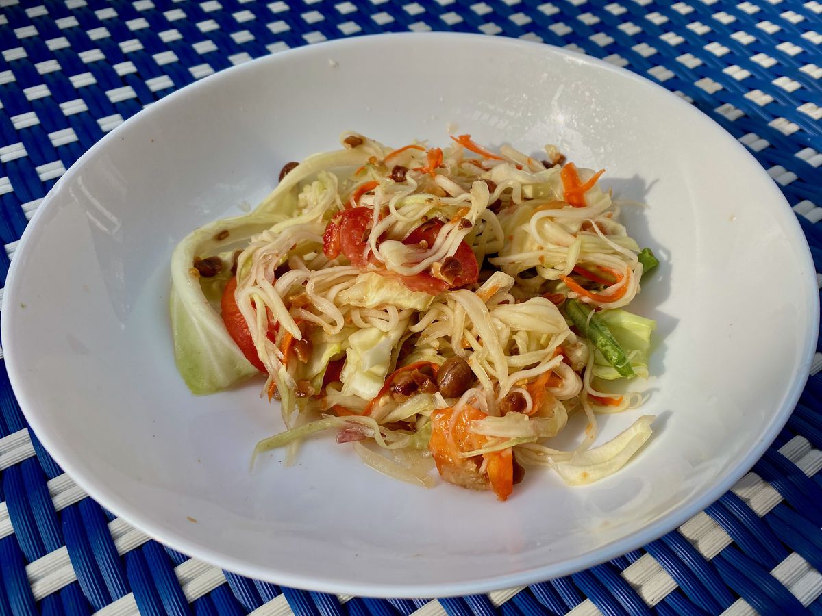 A white bowl filled with yellowish strips of papaya mixed with red tomatoes and green cabbage