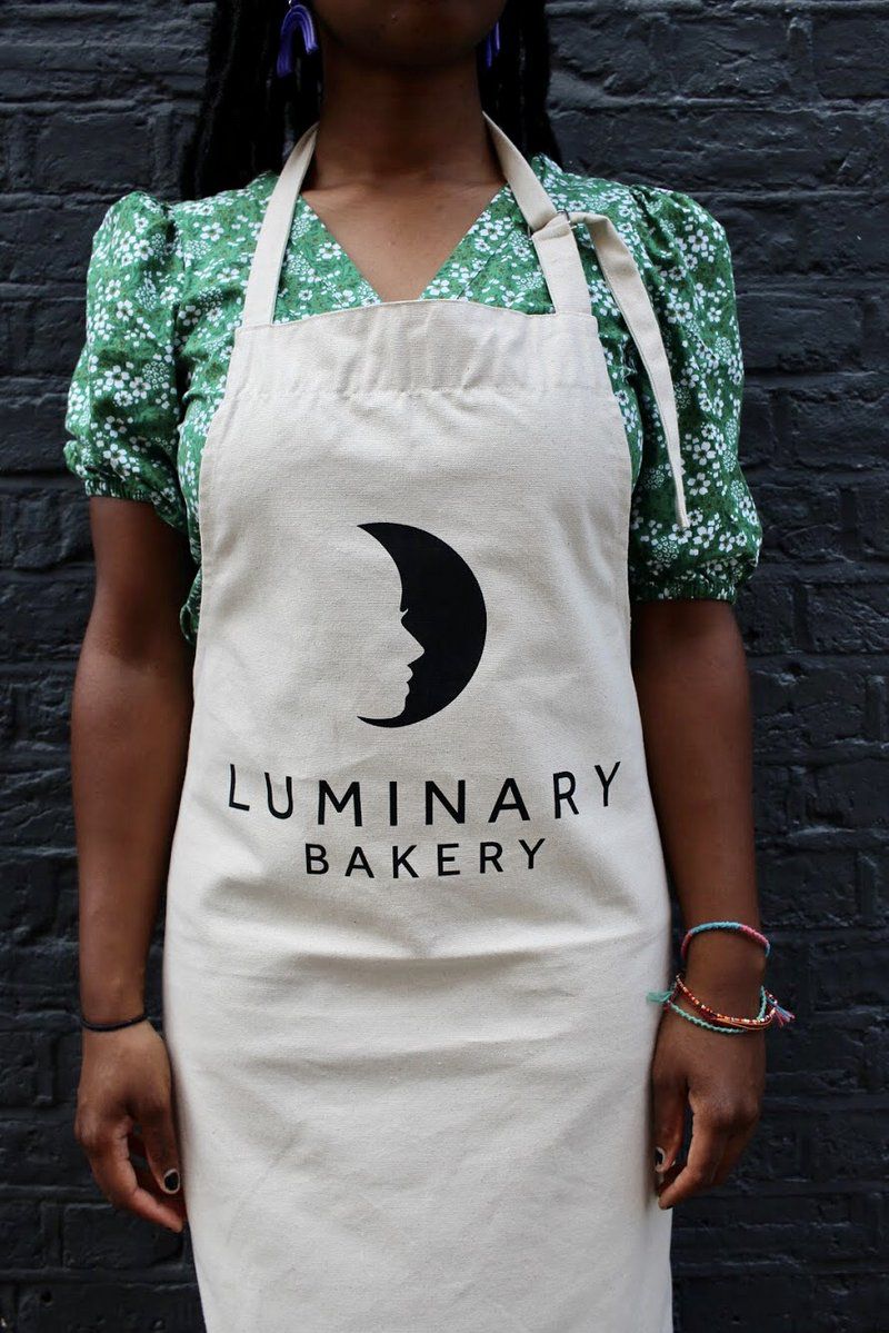 A Black female model wears the Luminary bakery apron