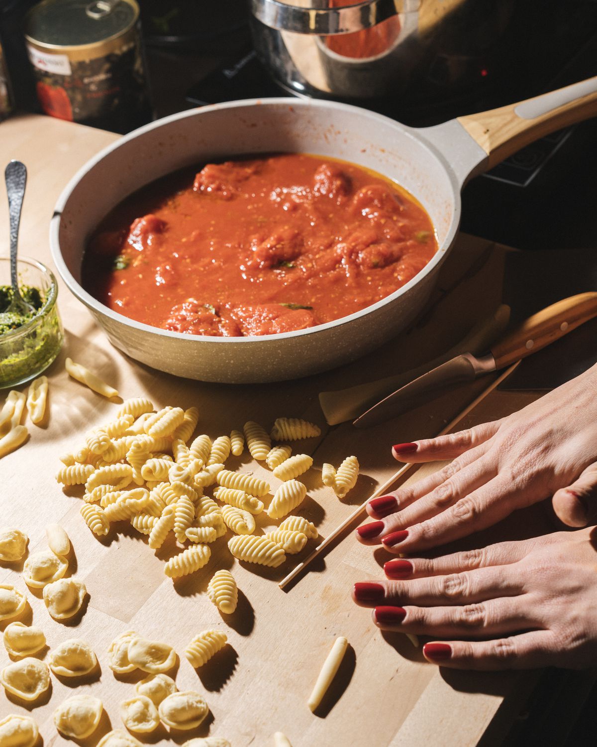 Two hands with red nail polish roll pasta with a pot with red sauce on the side.