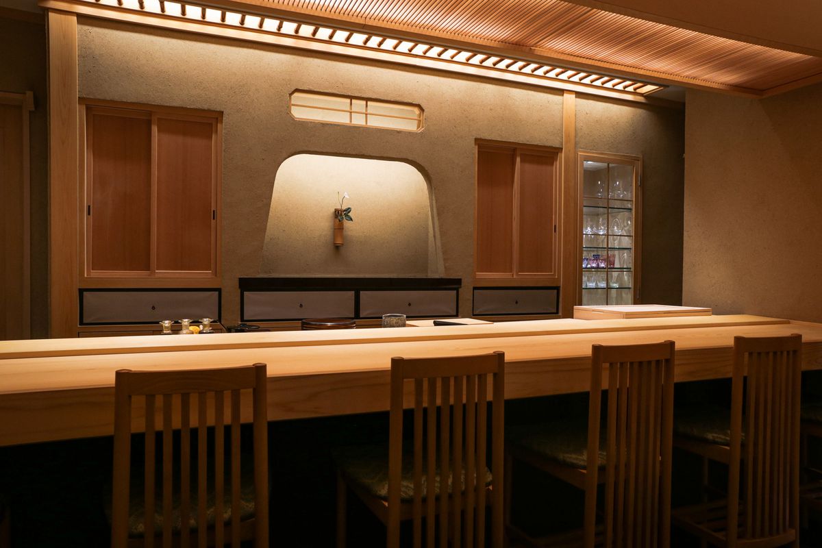 An interior photo of a light wood sushi bar with soft lighting.