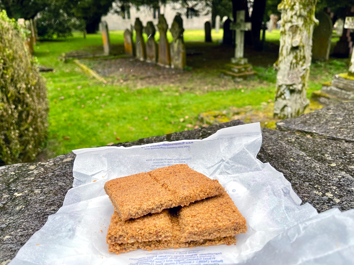 A small pile of gingerbread sitting on a stone wall with a graveyard beyond. 