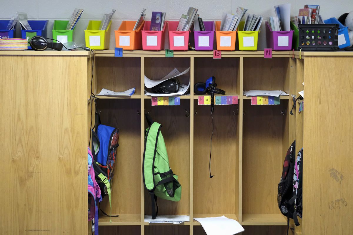 Multicolored file-holders sit atop four student cubbies holding papers, and backpacks in a classroom