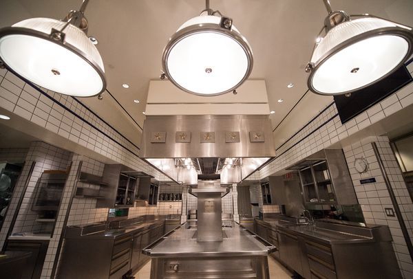 Per Se’s kitchen has three lights up top, white brick, and stainless steel counters.