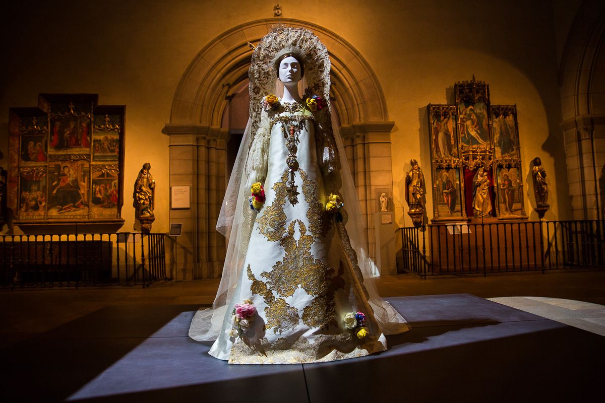 A mannequin wears an elaborate wedding dress covered in flowers and lace.