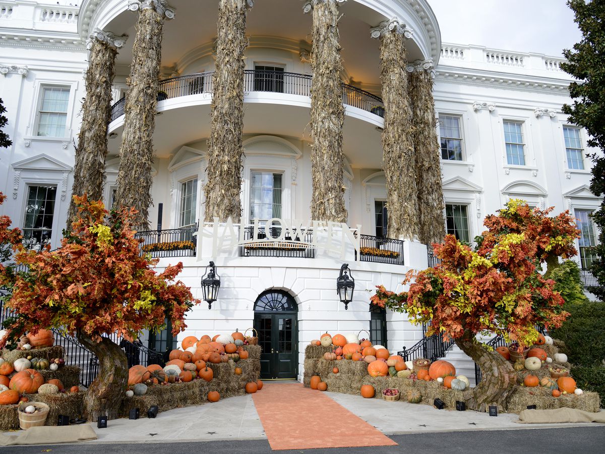A white federal-style mansion decorated with pumpkins and Halloween decorations.