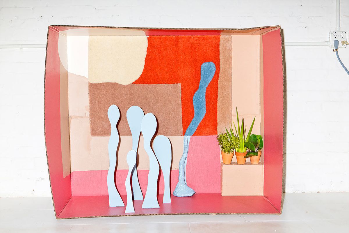 A rug with abstract shapes is placed within a cardboard diorama with its shapes appearing to bleed into physical forms outside of it.