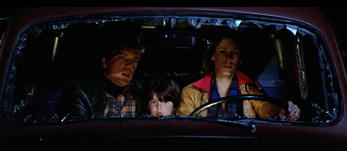 Elizabeth (Jamie Lee Curtis), Nick (Tom Atkins), and Andy (Ty Mitchell) look through a busted out windshield in a still from The Fog