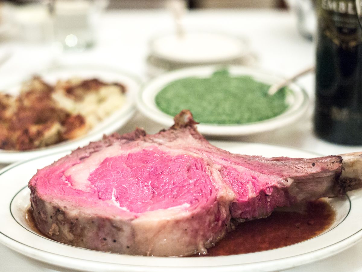 Medium rare prime rib on a white plate with creamed spinach in the background.