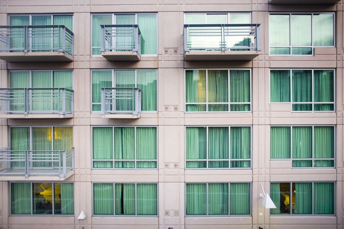 Three rows of floor to ceiling windows on the outside of a beige building with intermittent balconies.