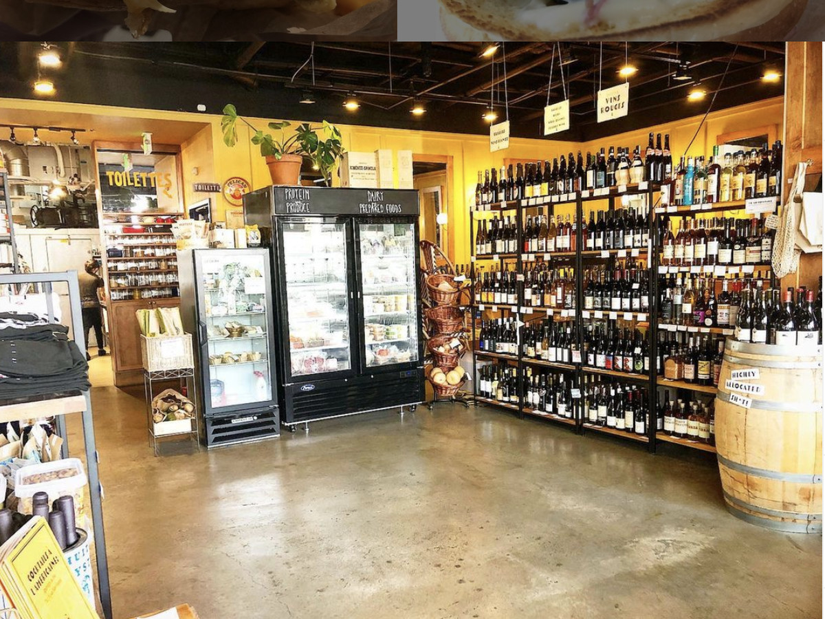 Shelves of wine and other bottles line the shelves at L’Oursin in Seattle, with a refrigerator in the center of the space