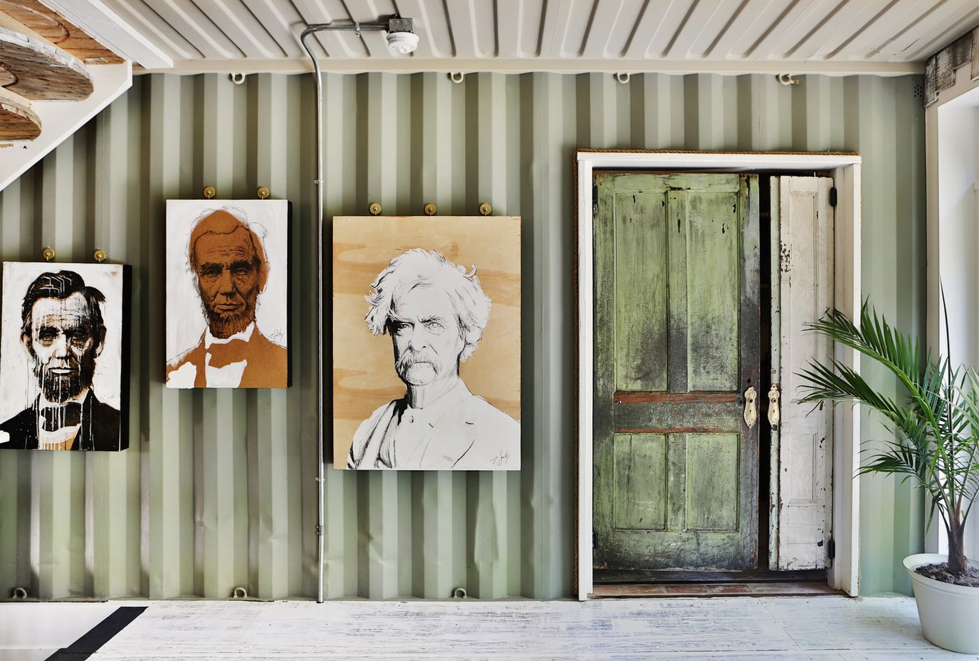 The couple who built the shipping container house left some metal walls exposed. Here, you see light-green metal walls and a white metal ceiling. Artwork by owner Zach Smithey, showing portraits of Abraham Lincoln and Mark Twain, decorates the walls.