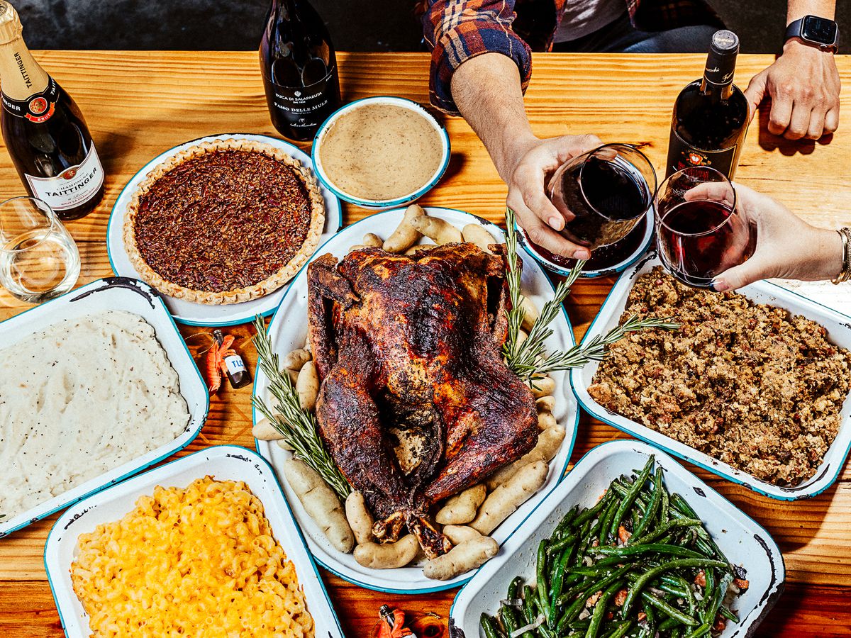 A Thanksgiving spread with turkey on a plate surrounded by side dishes in aluminum tins