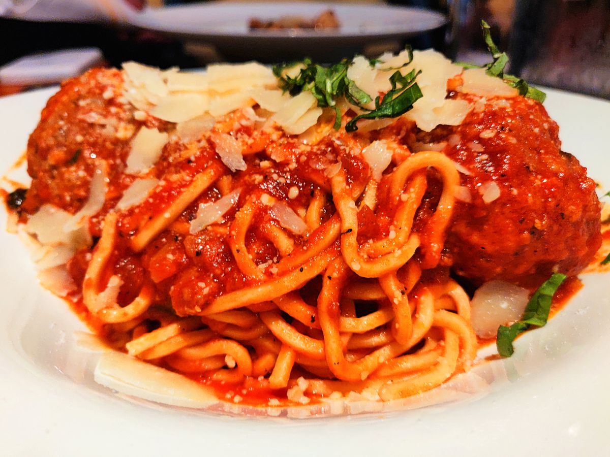 Closeup on a dish of spaghetti in red sauce with large meatballs and thickly grated cheese.